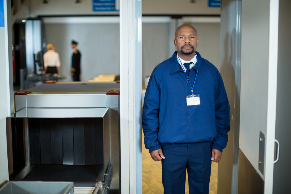 portrait of airport security officer standing in metal detector door at airport terminal